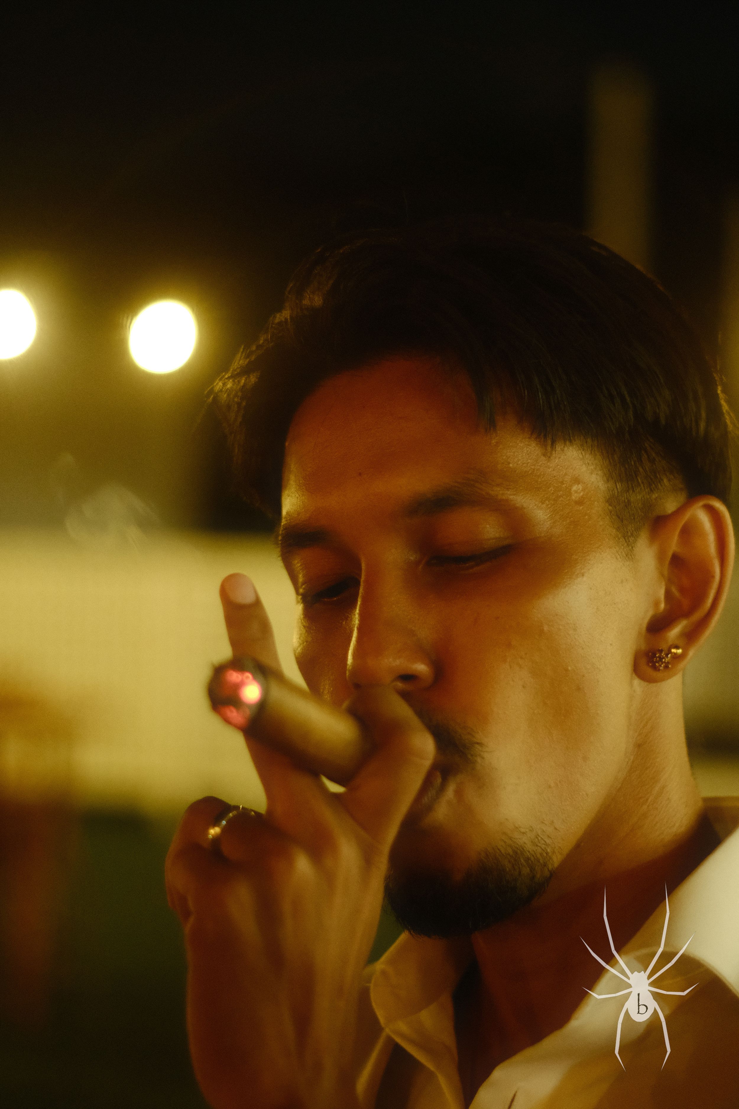 Person smoking illuminated by warm ambient lights in a dark setting with a spider watermark.