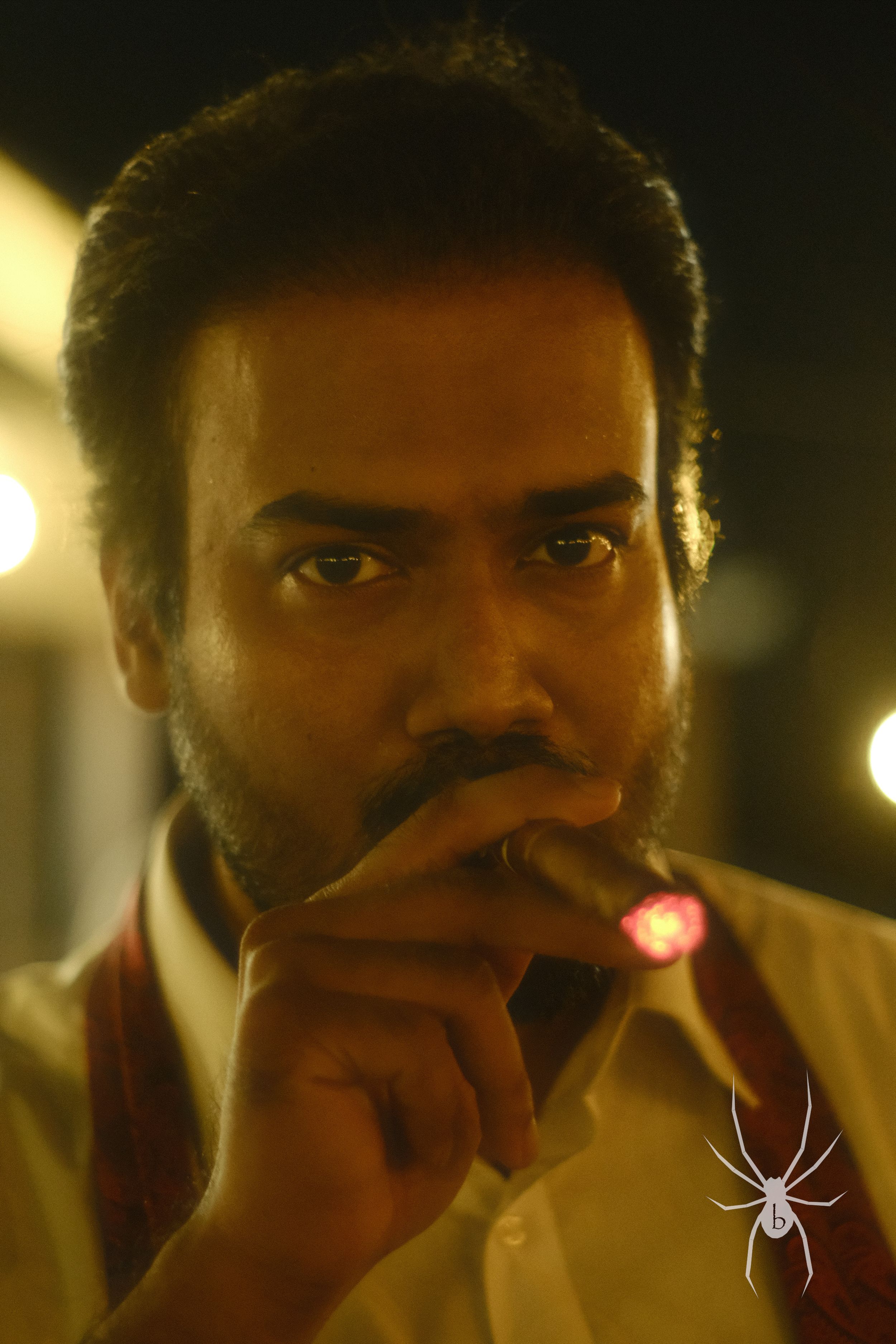 Dramatic portrait of a person with facial hair in warm lighting holding something near their mouth.