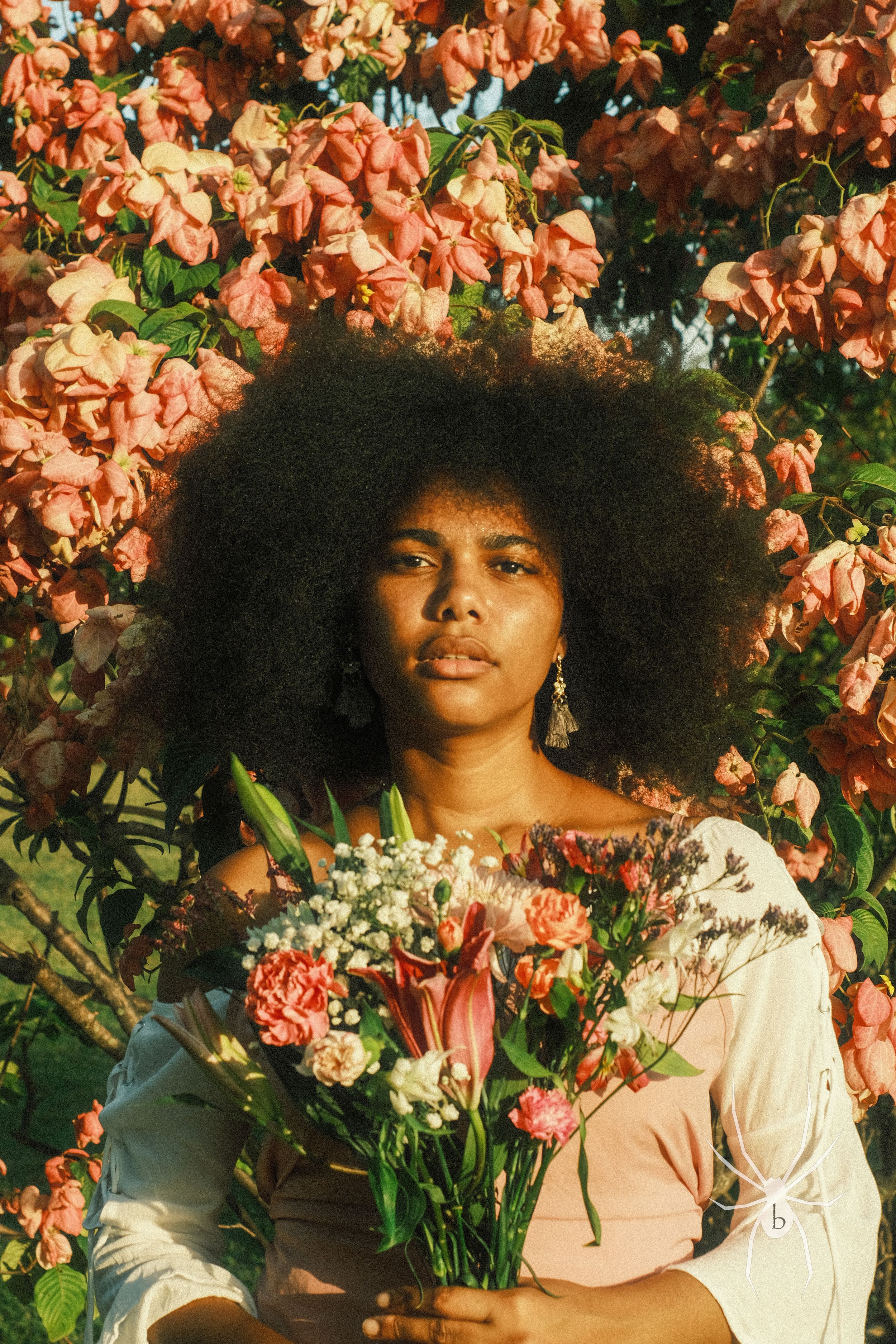 Natural portrait among coral-colored flowers with a bouquet and a spider watermark in the corner.