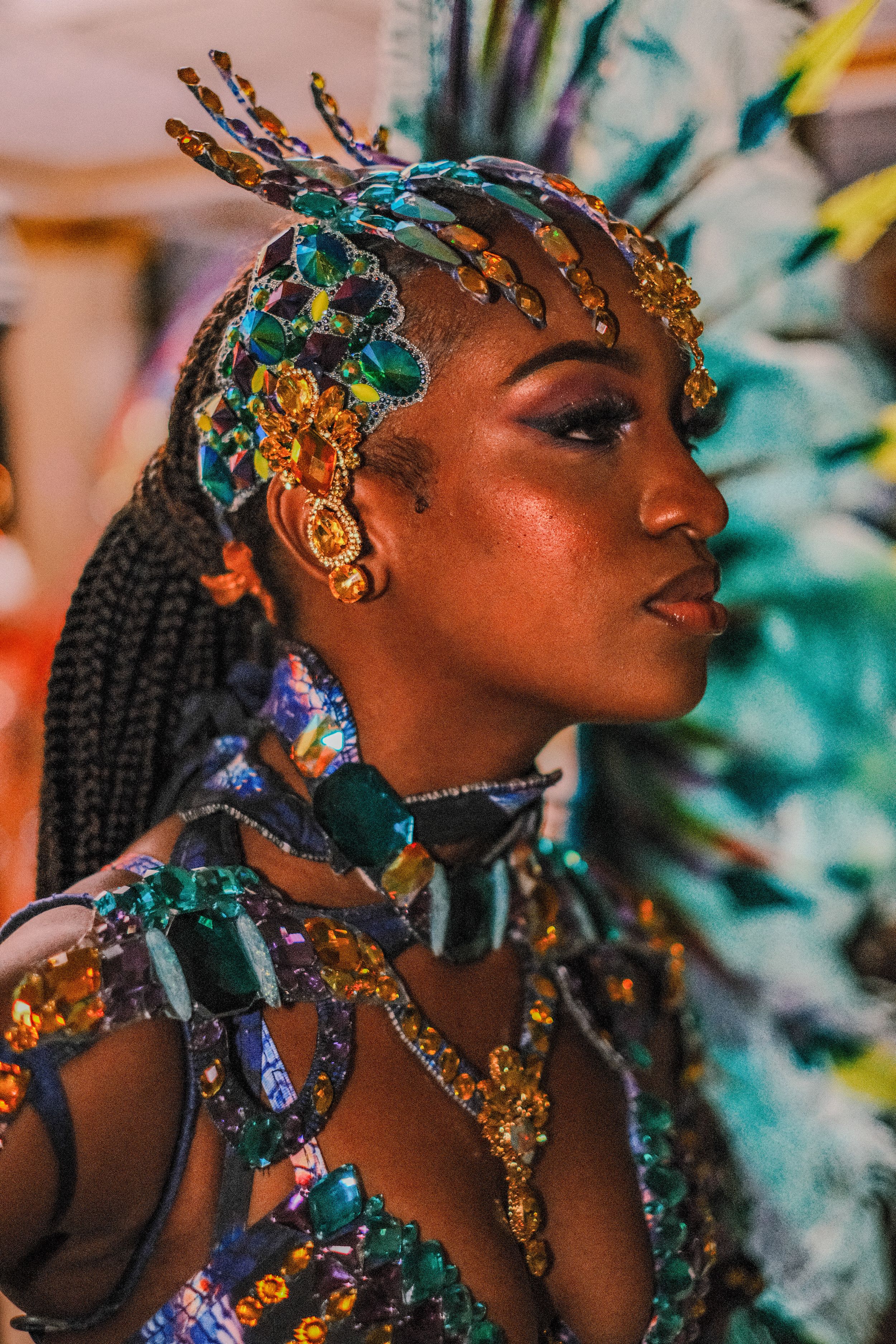 Carnival performer wearing elaborate turquoise and gold headdress with colorful feather accessories.