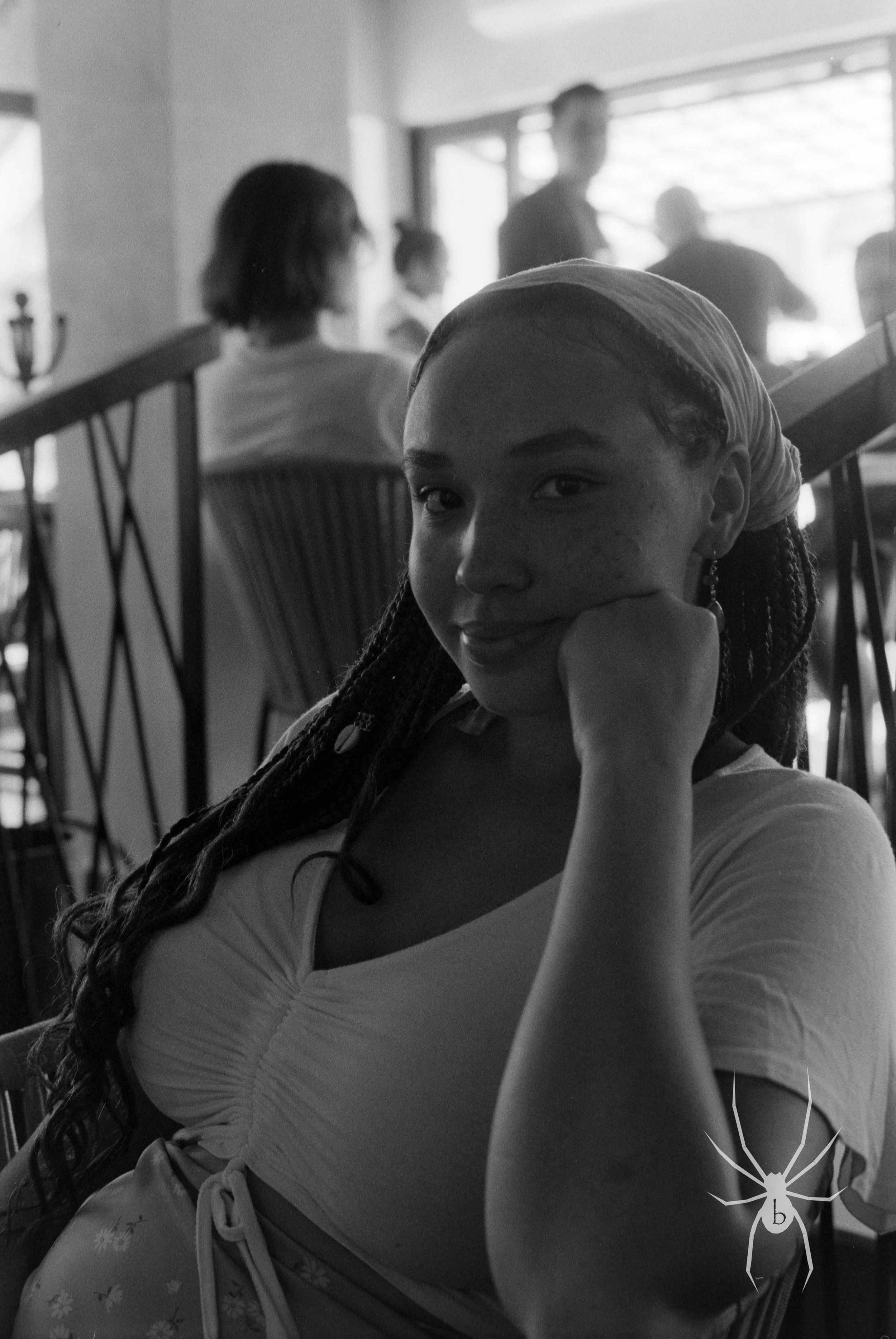 Black and white indoor portrait of a person with braided hair resting their head on their hand.