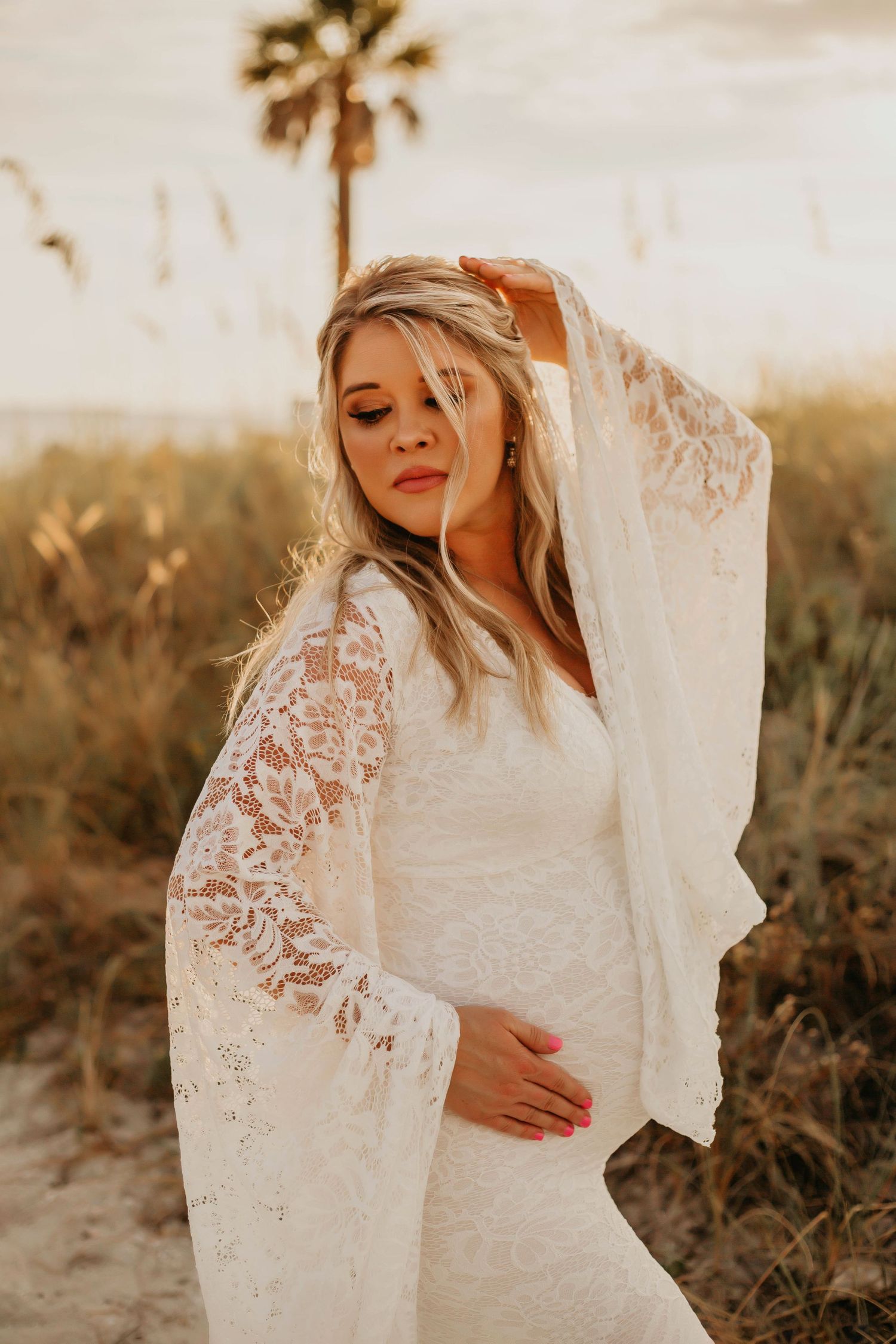 A bride in a lace wedding dress poses at sunset with a palm tree in the background.