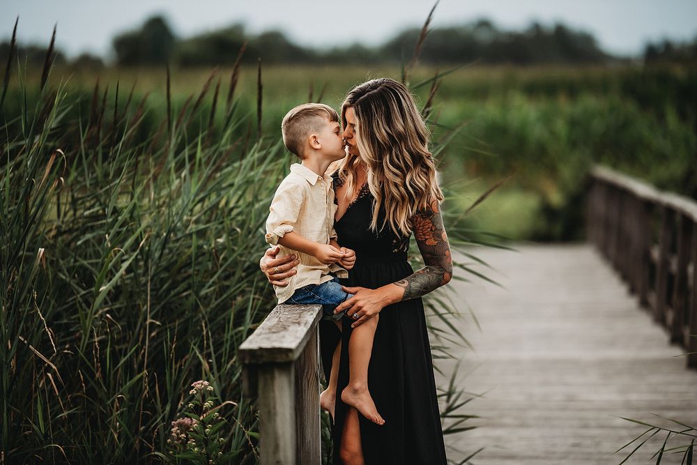 Tender moment captured on a wooden boardwalk surrounded by tall marsh grasses at golden hour.