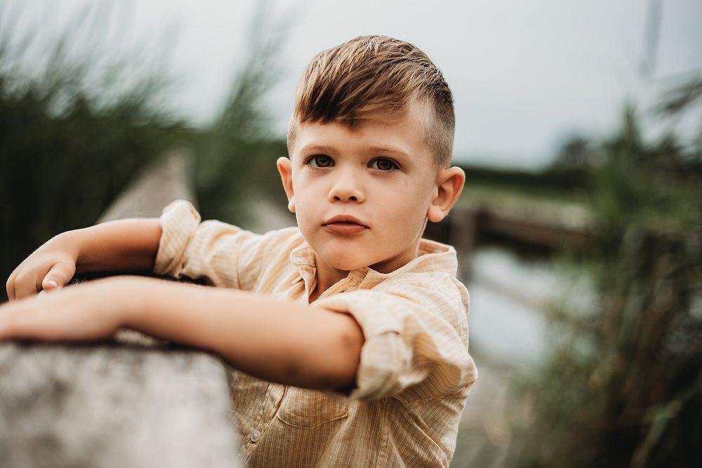 Close-up portrait of a young boy in beige shirt leaning on a railing outdoors.