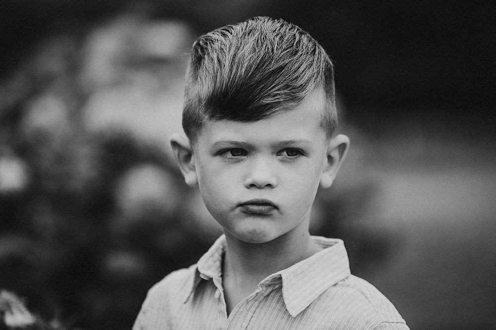 A dramatic black and white portrait of a young child wearing a collared shirt.
