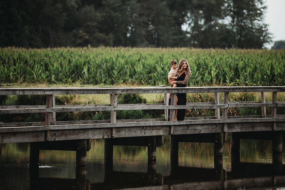 A pair share an intimate moment on a wooden bridge surrounded by cornfields.