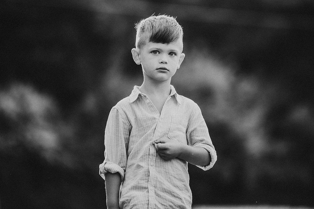A black and white portrait of a young child in a button-down shirt looking at the camera.
