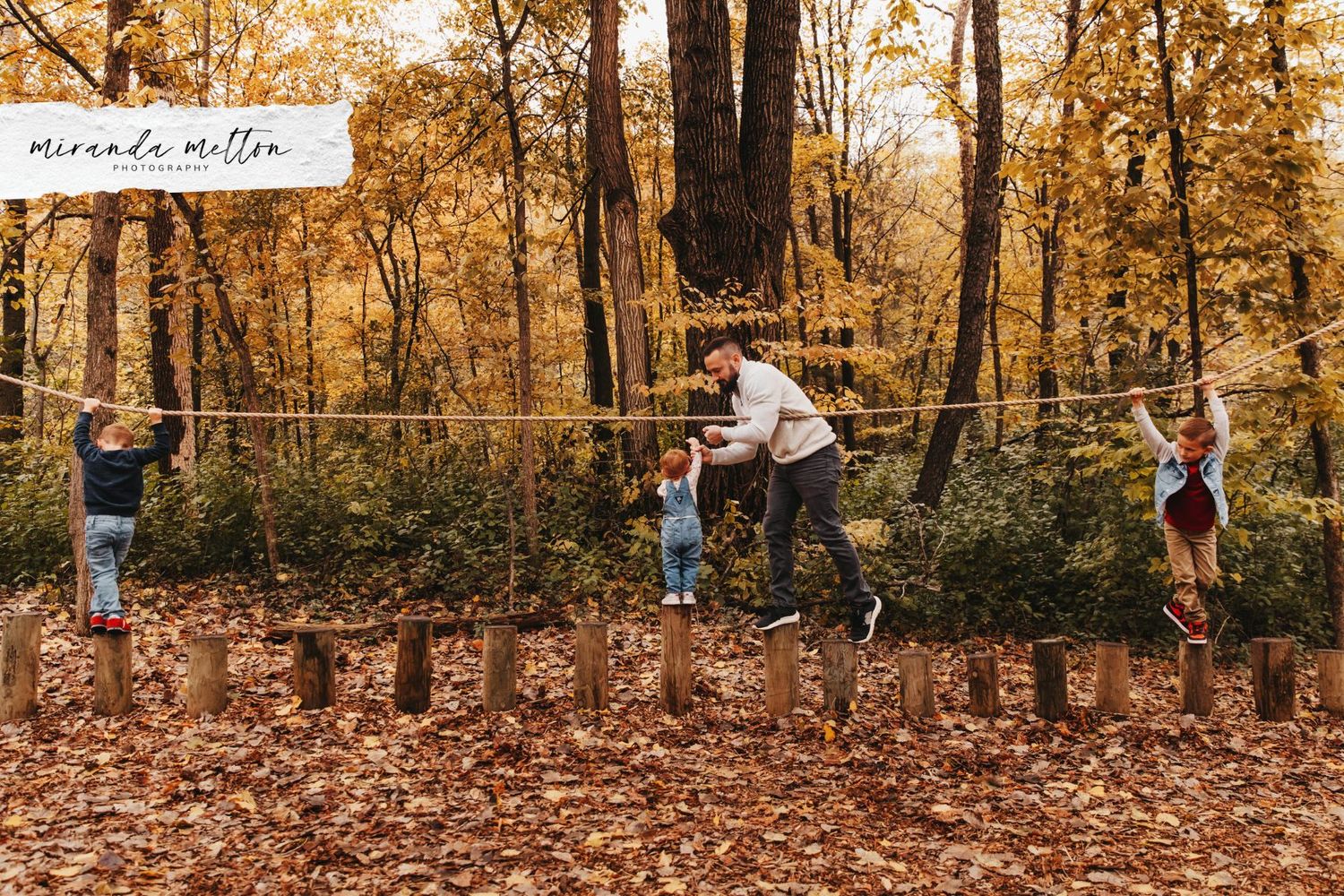 A dad and his 3 kids play together on a natural play structure in Savage, MN. Photo highlights the best places to take family photos in MN.