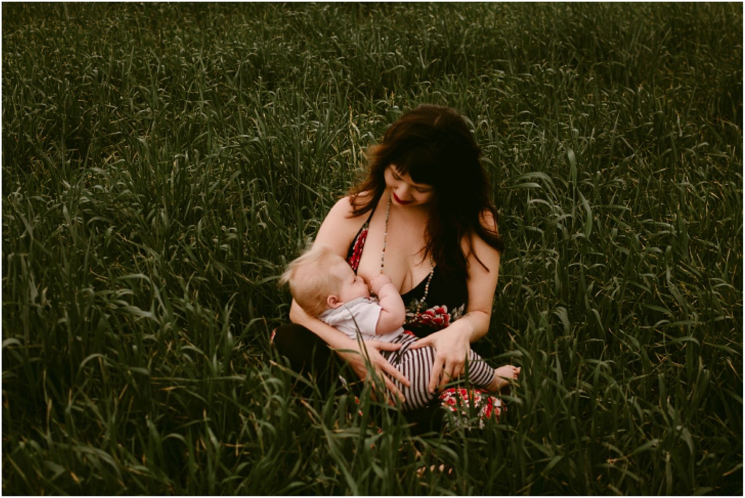 Intimate nursing session captured in tall grass during golden hour.