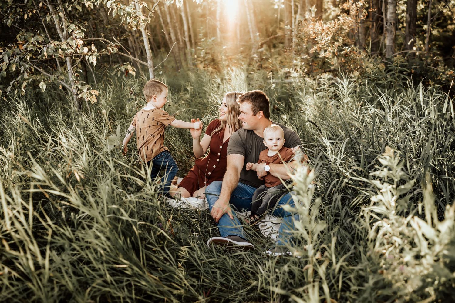 Romantic outdoor photoshoot in tall grass with golden sunlight filtering through trees.