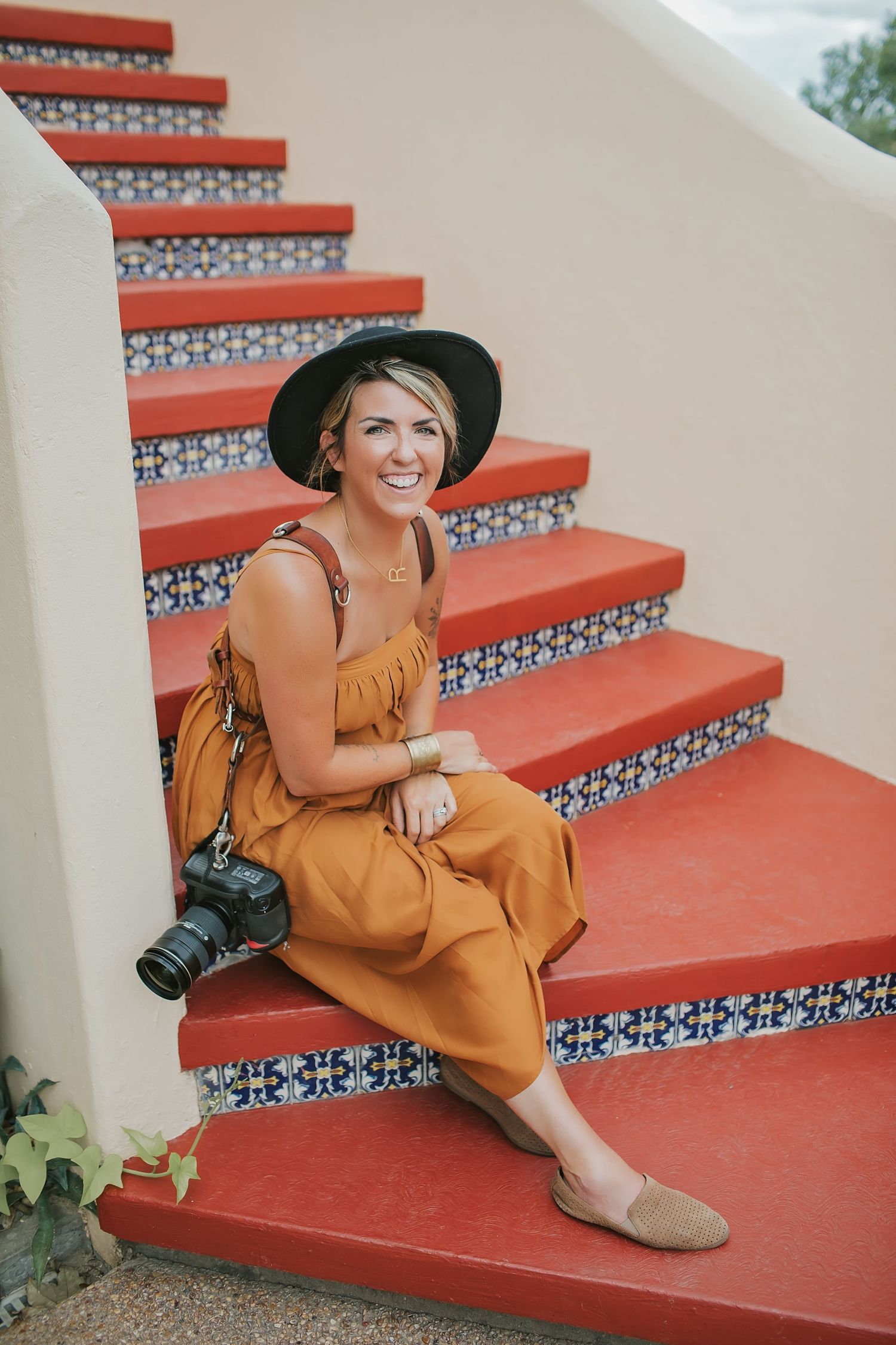 A person in an orange dress and hat sits on decorative red stairs with a camera.
