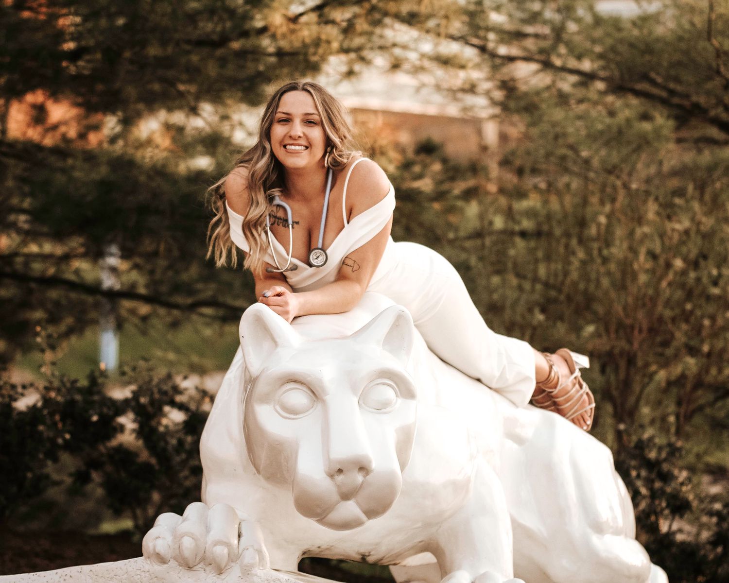 A person in white poses on a decorative stone lion statue outdoors.