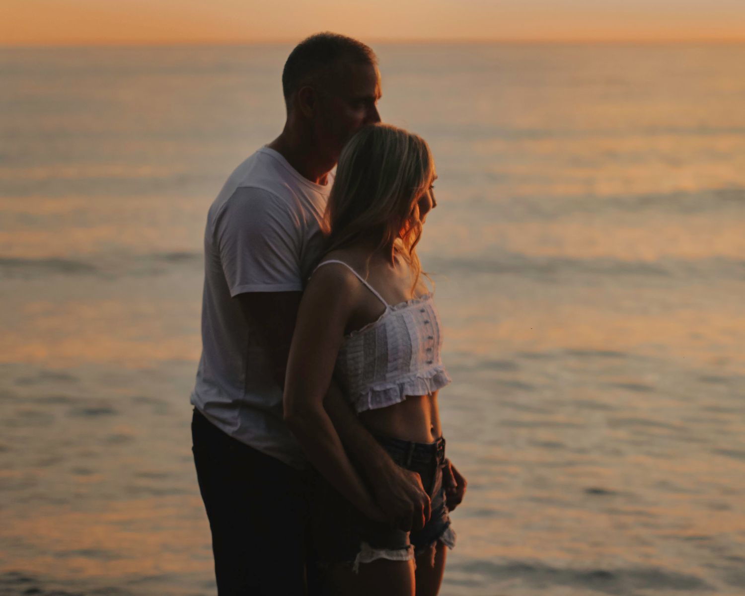 Silhouetted couple embracing during golden hour sunset by the water.
