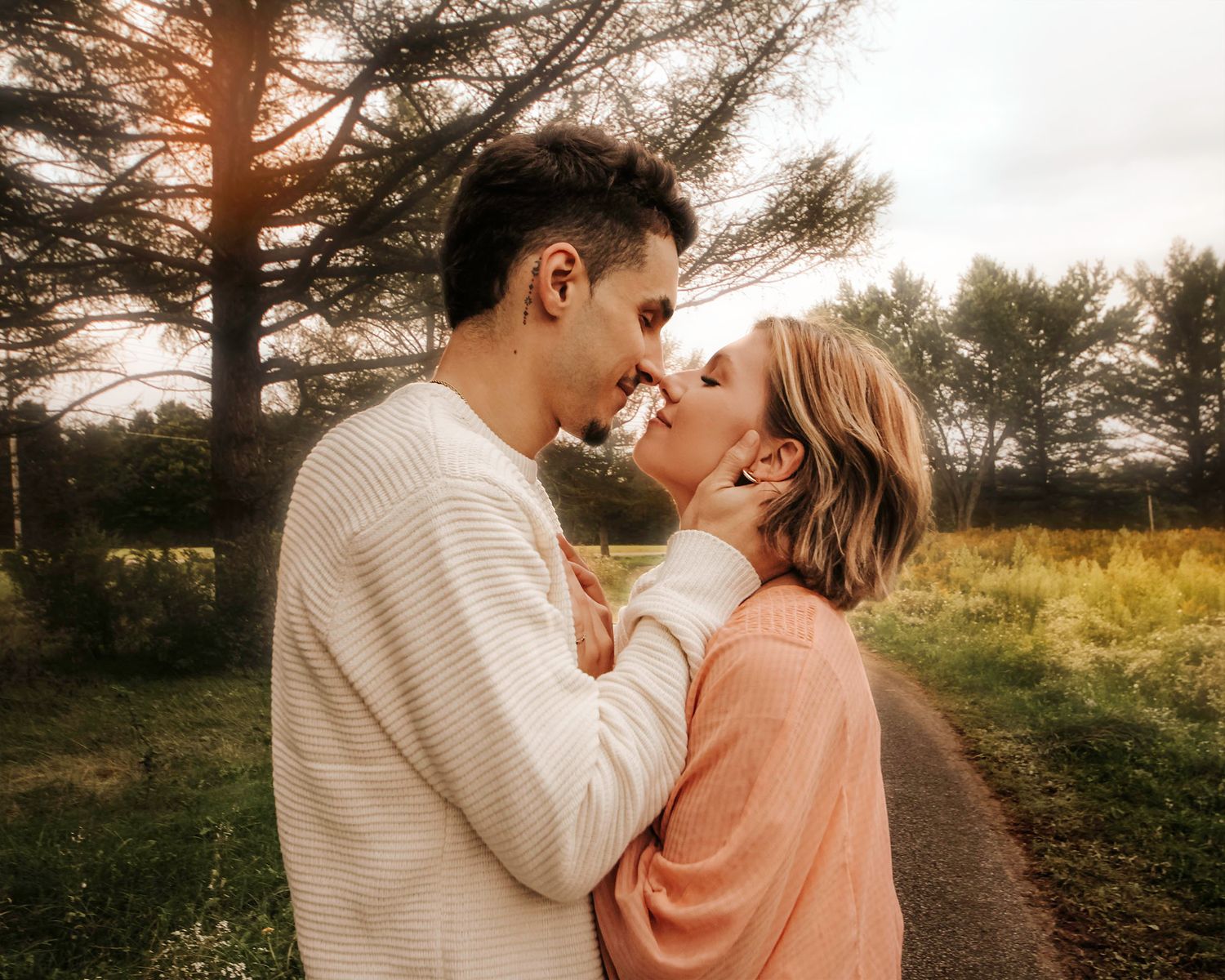 Romantic sunset photography session with couple in cream and peach sweaters among pine trees.