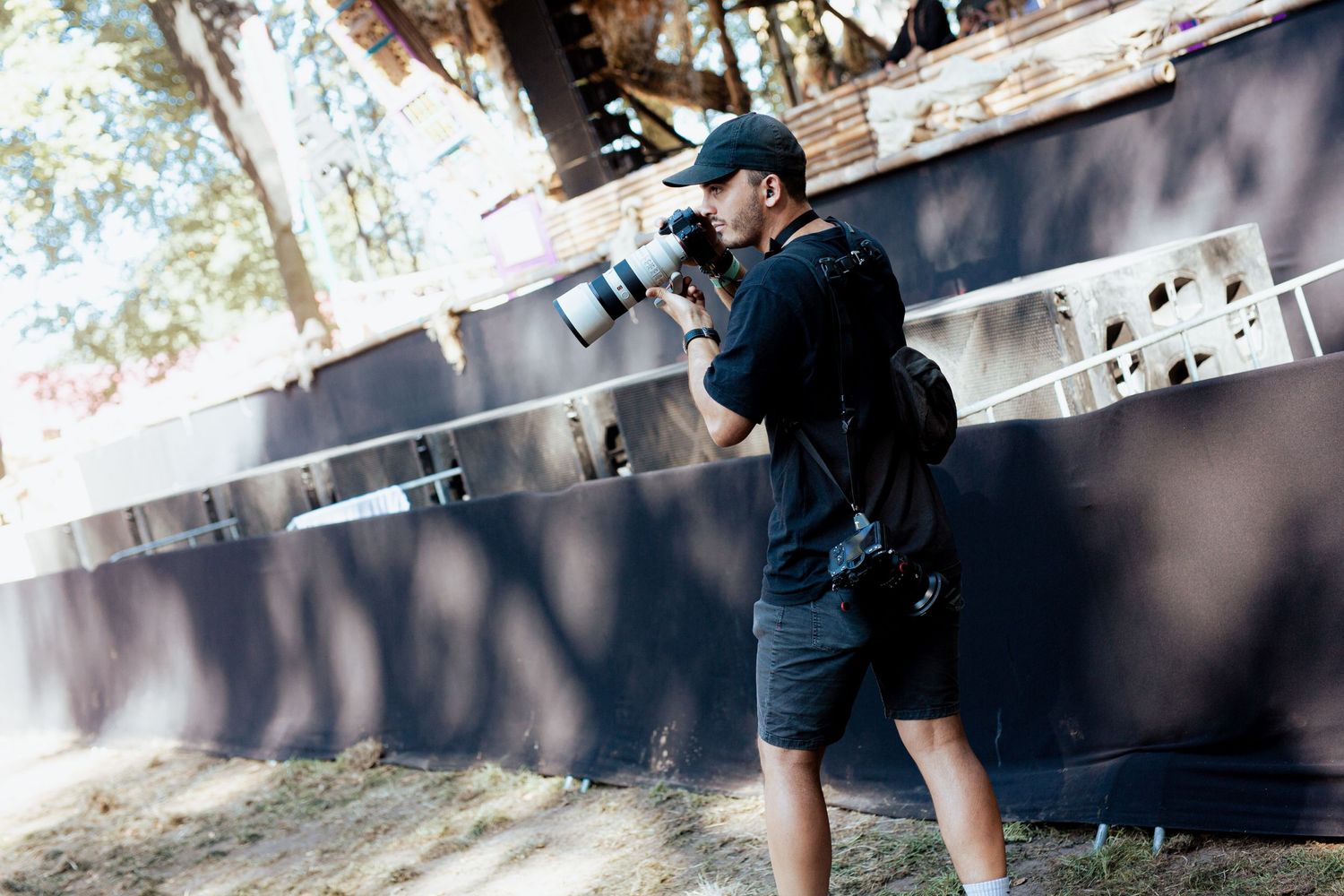 Photographer in dark clothing taking photos against concrete wall outdoors.