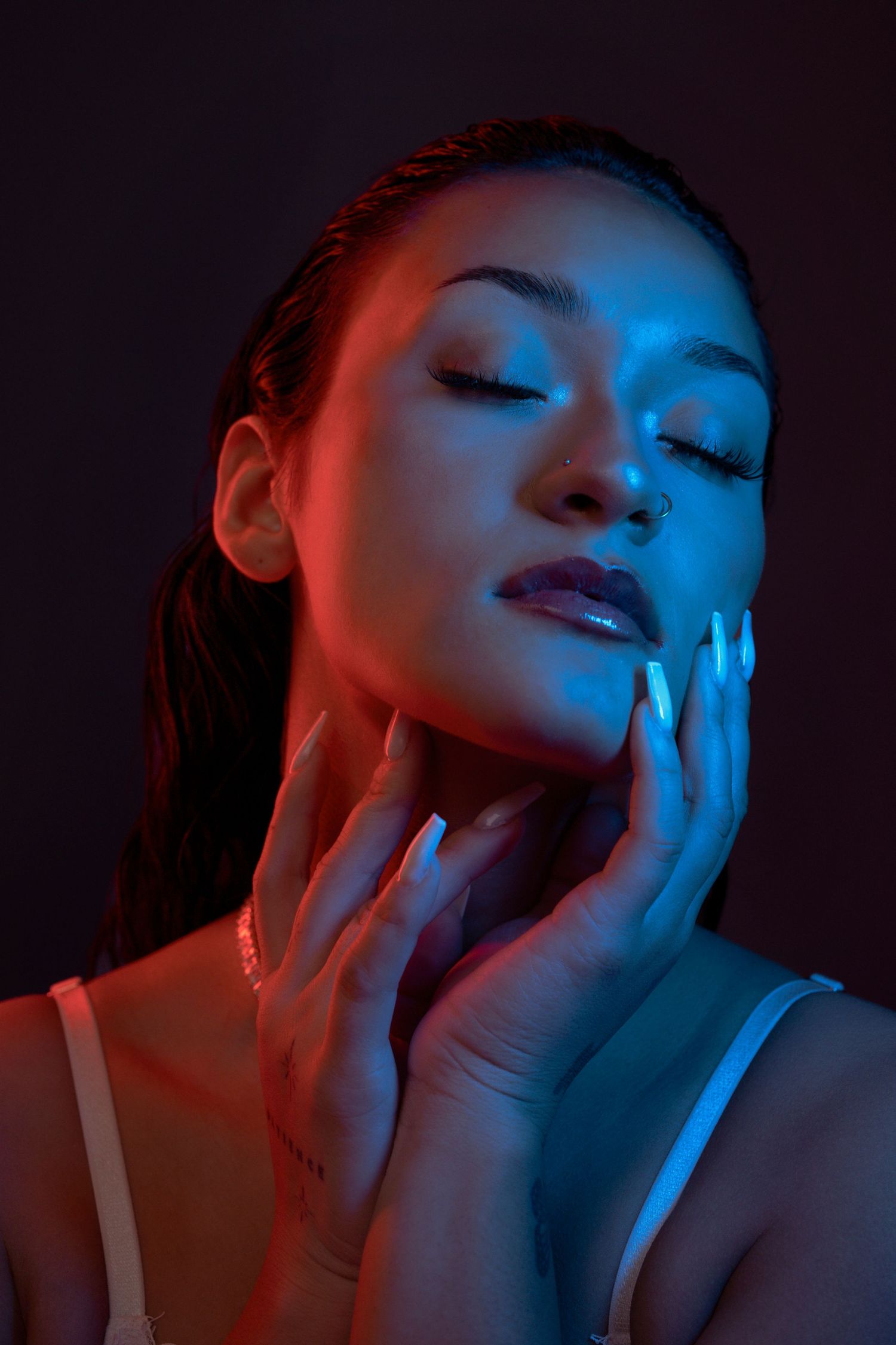 Artistic portrait with neon lighting showing closed eyes and delicate hand placement.