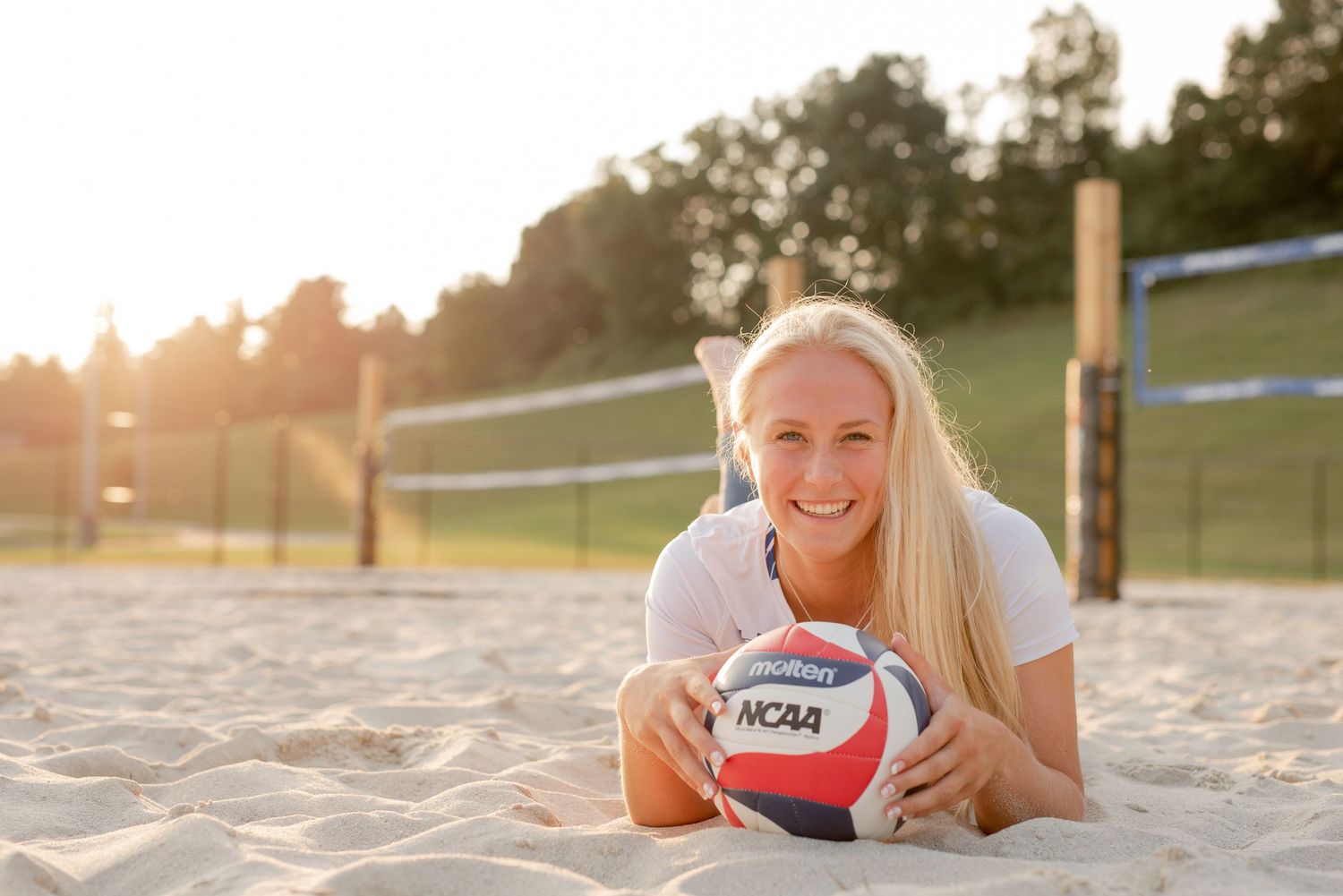Beach volleyball player poses with ball on sandy court during golden hour sunset.