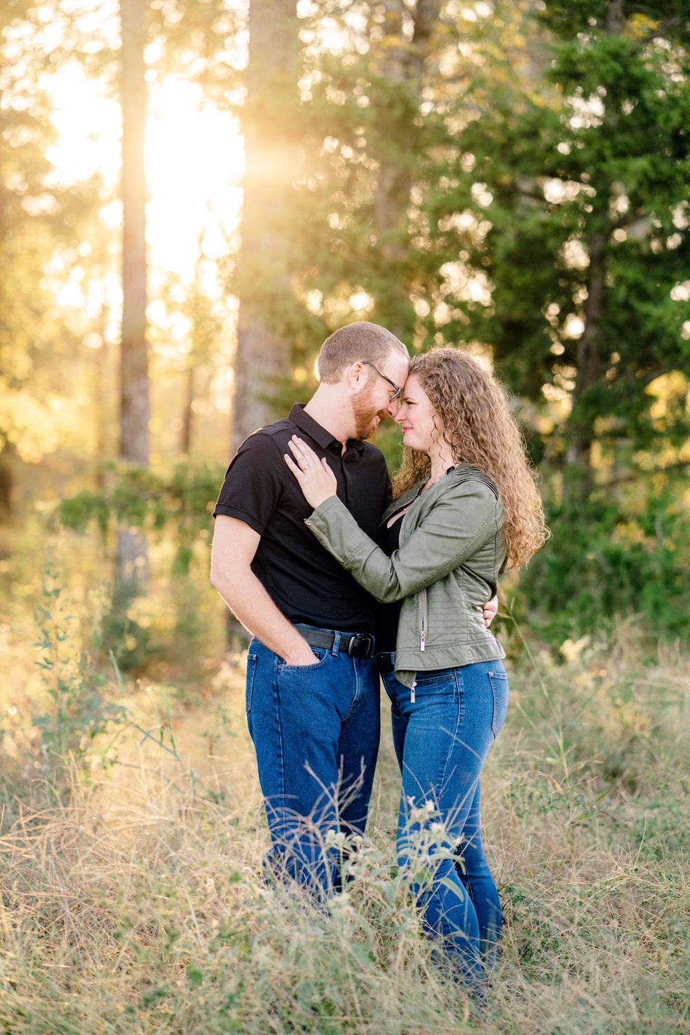 Intimate portrait of a couple embracing in a sun-dappled forest clearing.