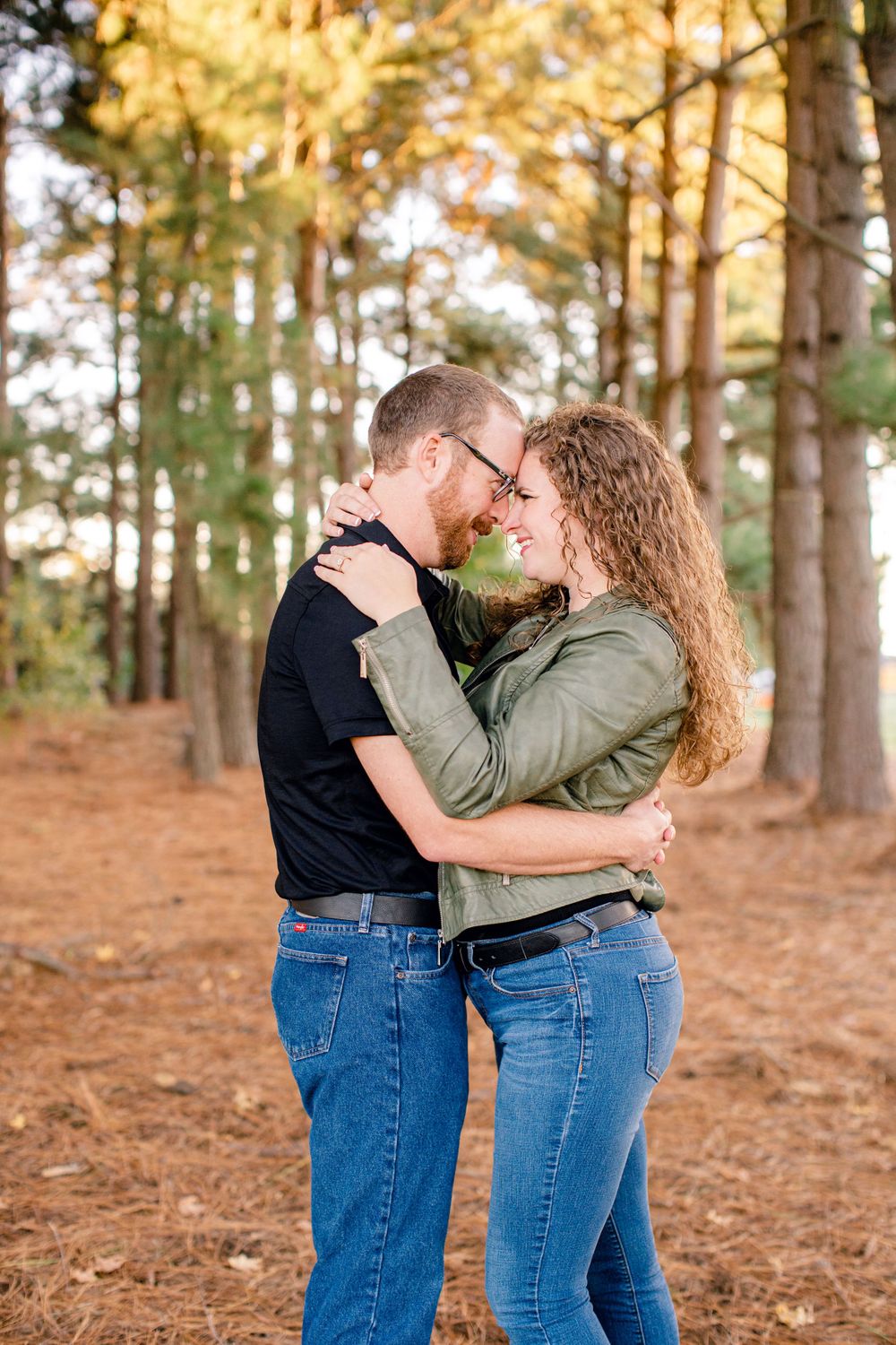 A couple shares an intimate embrace while standing on pine needles in an autumn forest at golden hour.