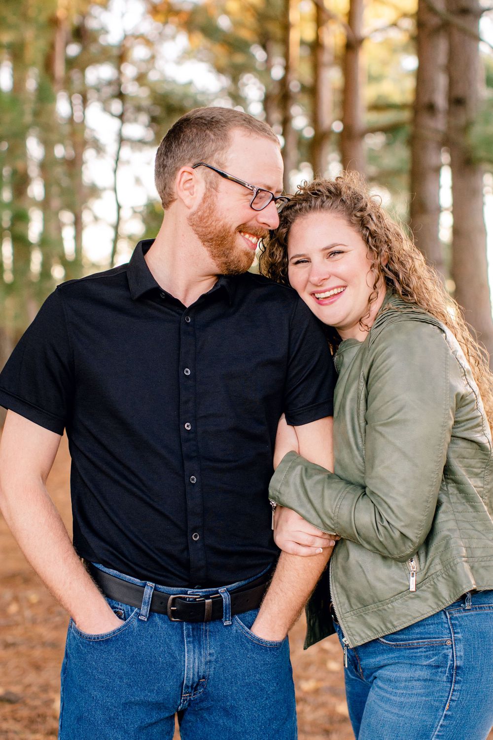 A couple shares a joyful moment together in a sunlit pine forest.