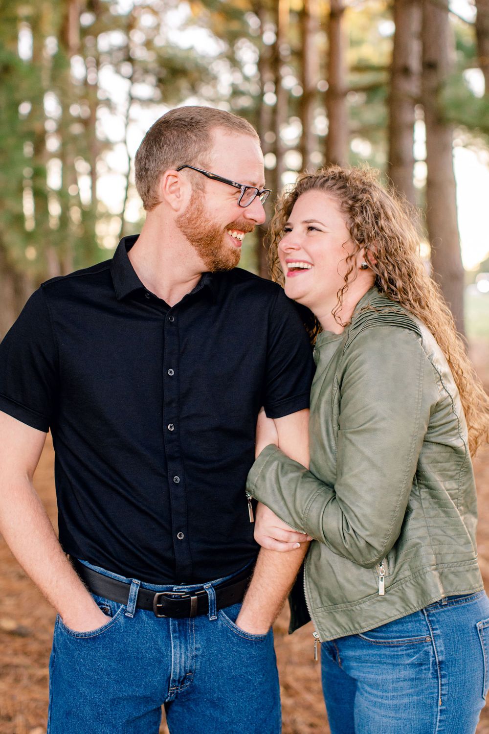 Couple laughing together during an autumn photoshoot in a wooded setting.