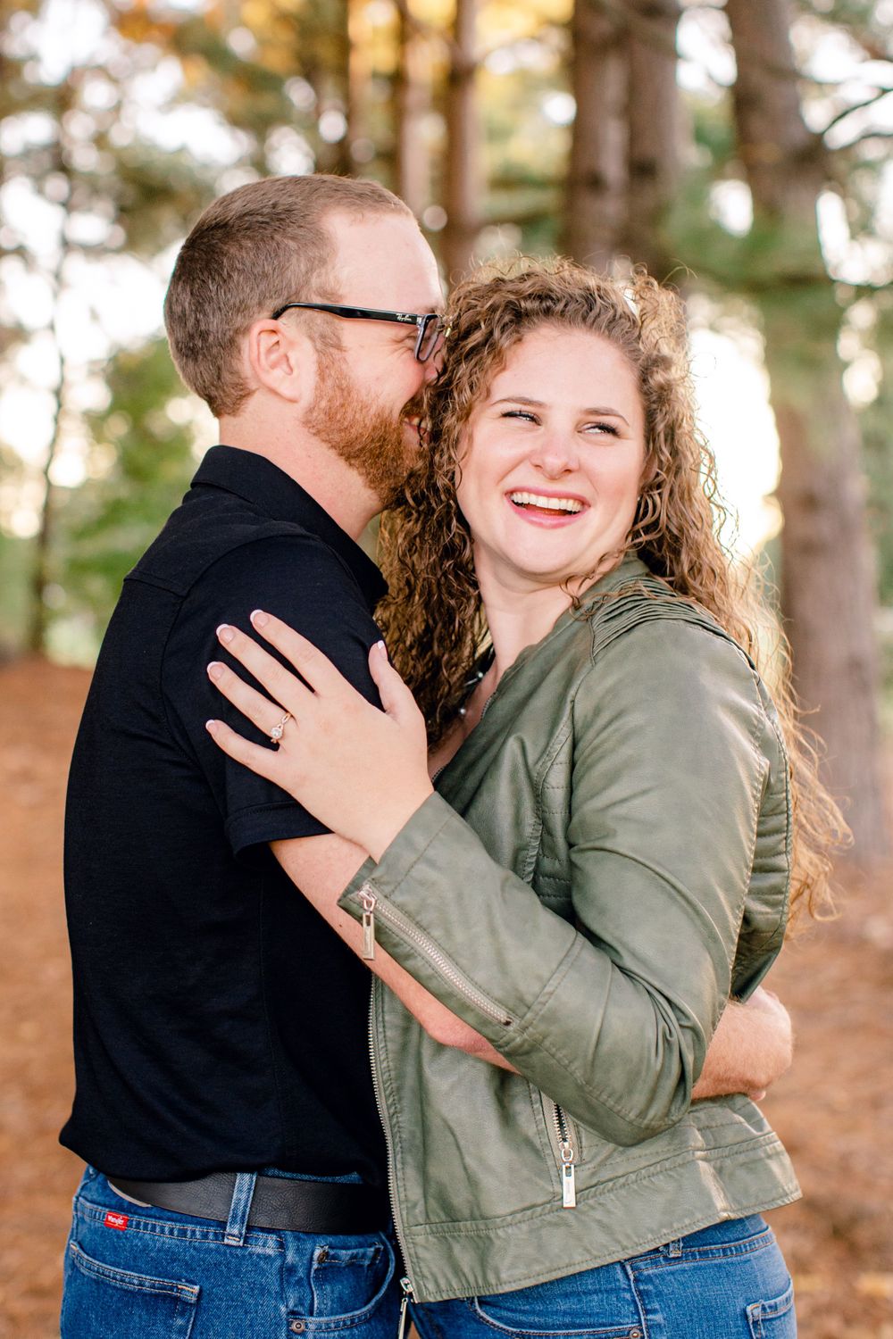 Couple embracing and laughing together in a sunny forest setting.