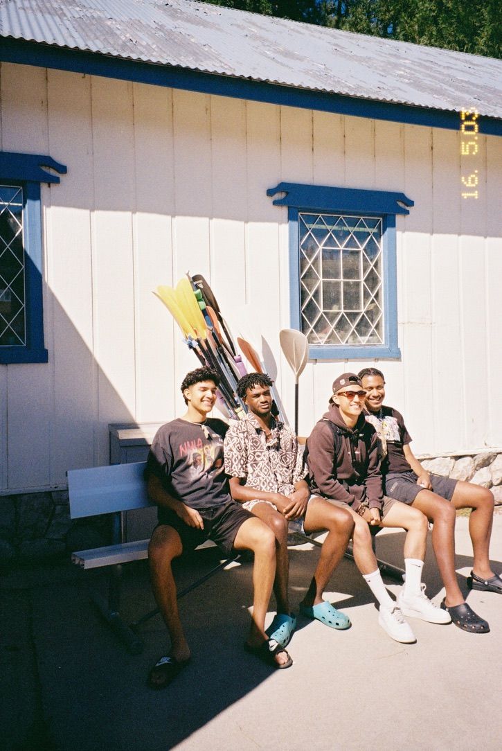 Group sitting outdoors on a bench against white building with blue trim.