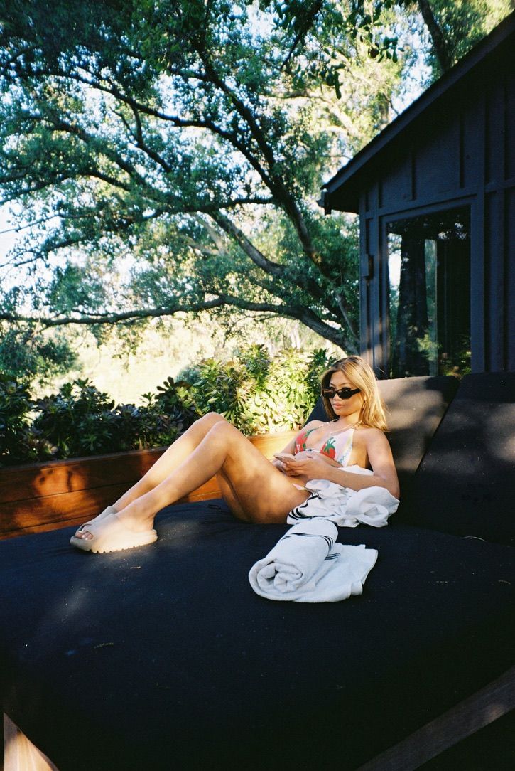 Person relaxing and reading on a deck with trees in the background.