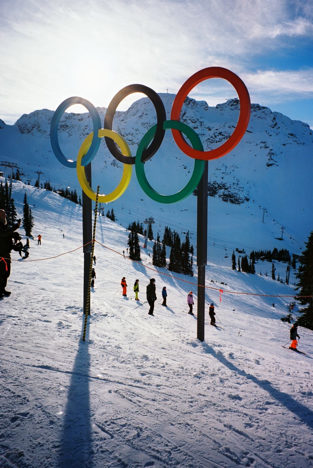 Olympic rings displayed on snowy ski slope with mountain backdrop.