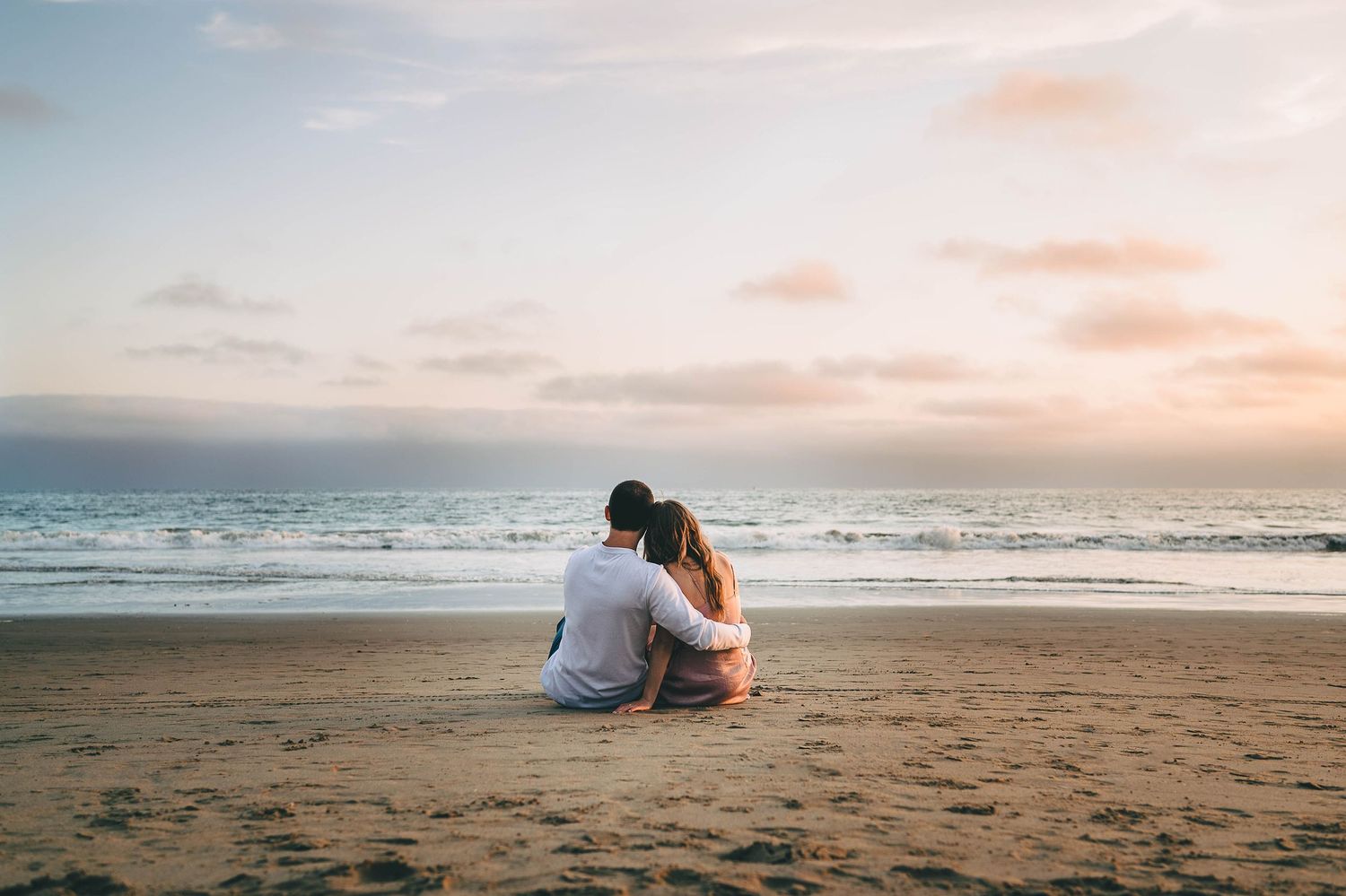 Couple sits together watching sunset on peaceful beach shoreline.