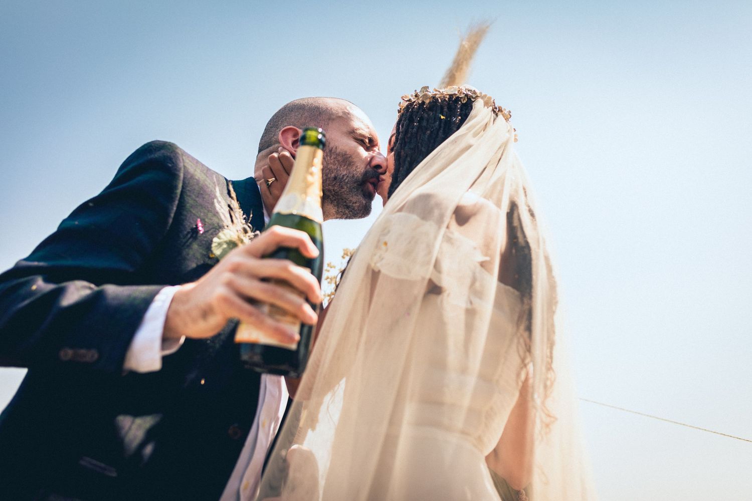 Newlyweds sharing a romantic moment while holding champagne glasses outdoors.