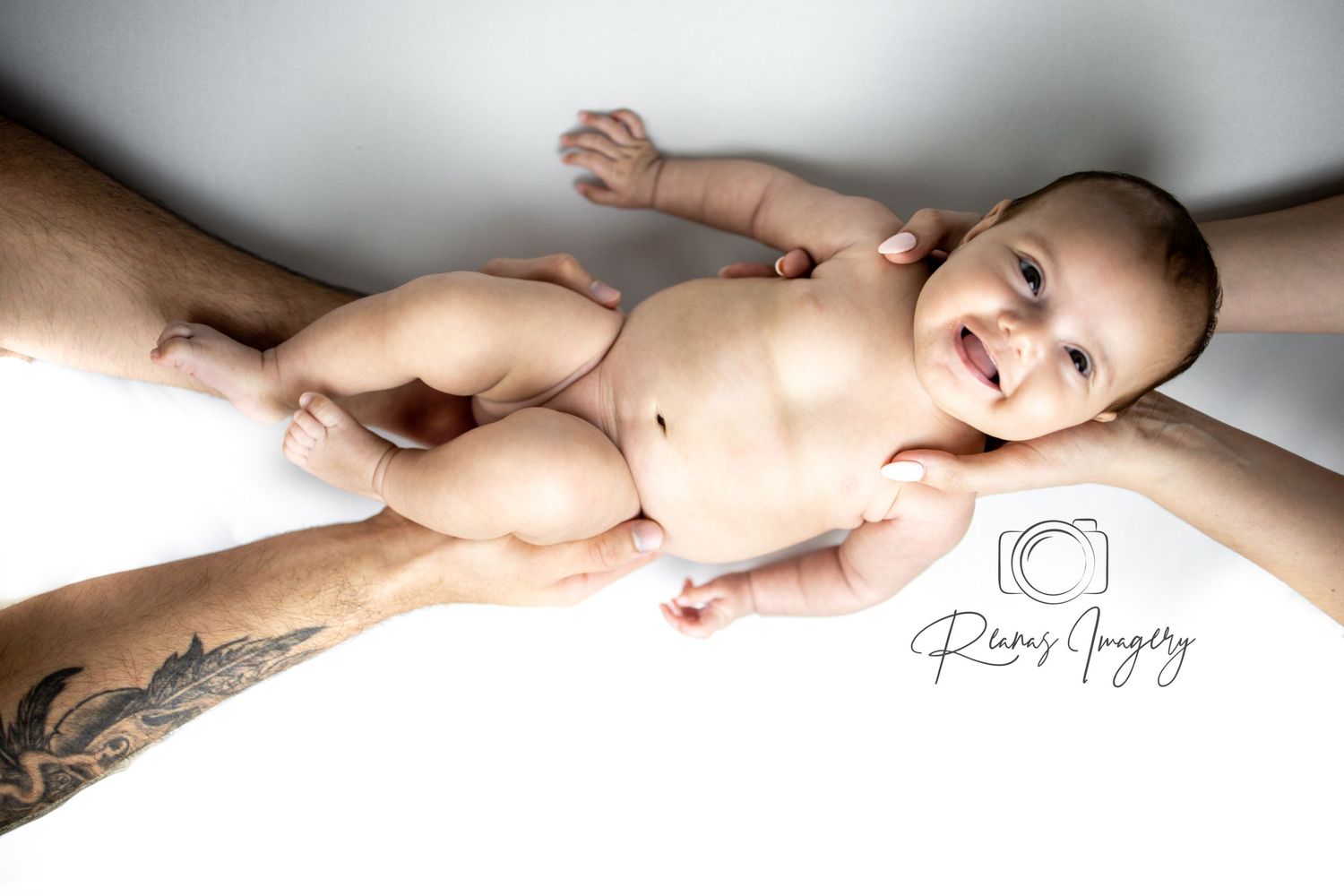 Newborn baby smiles while being gently supported by parents hands in studio portrait.