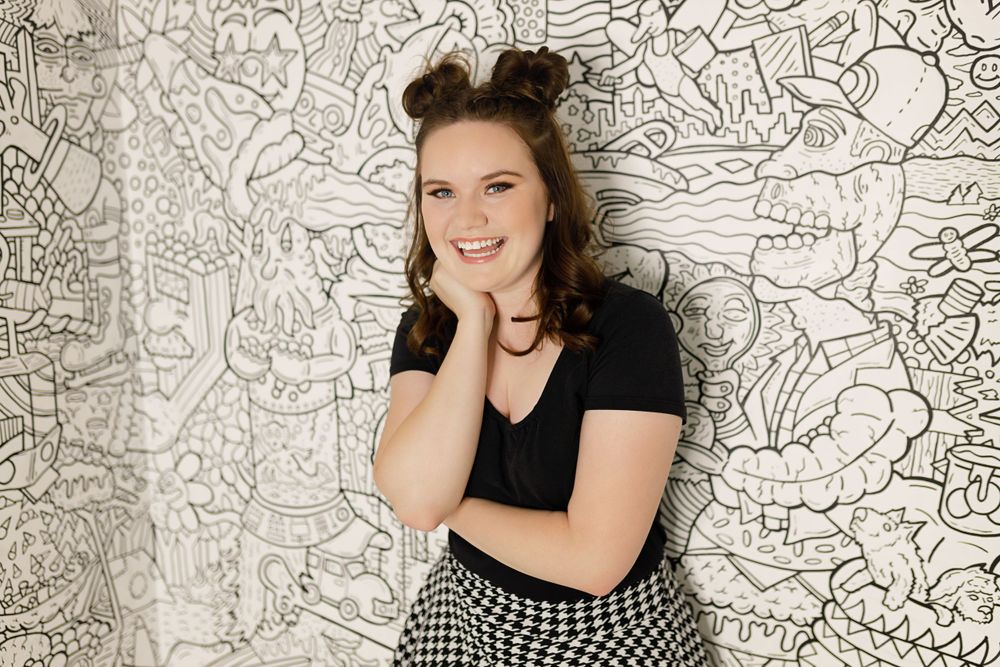Portrait against patterned wall shows woman in checkered pants and black top.
