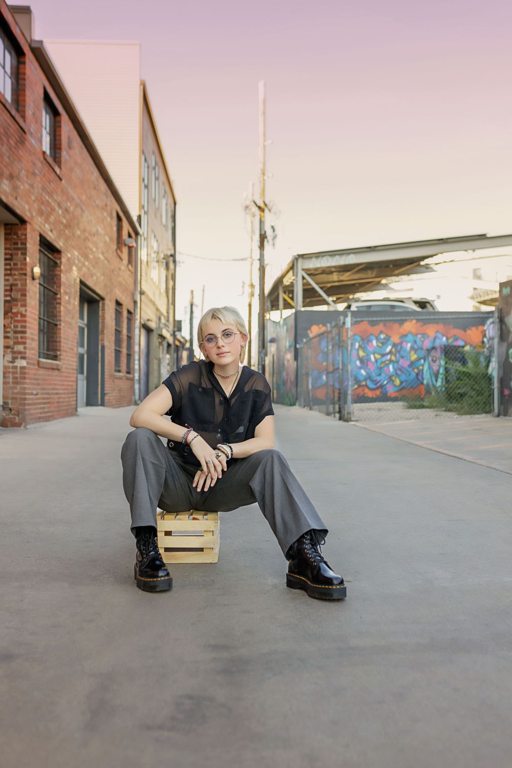 Urban photo session with graffiti background and industrial setting as subject sits on wooden crate.