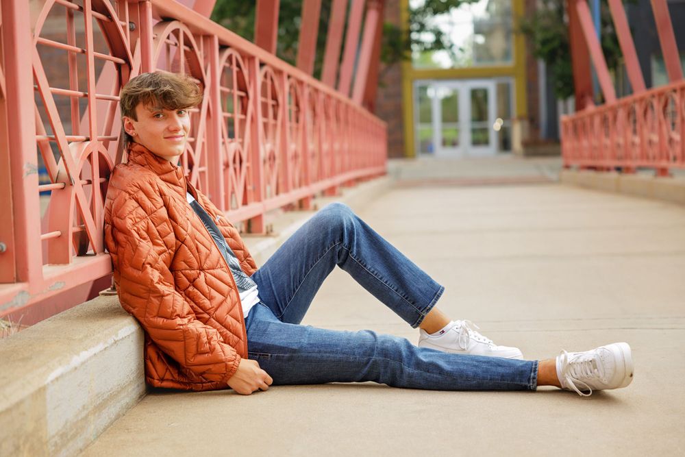 Person in orange jacket reclines on red bridge walkway.