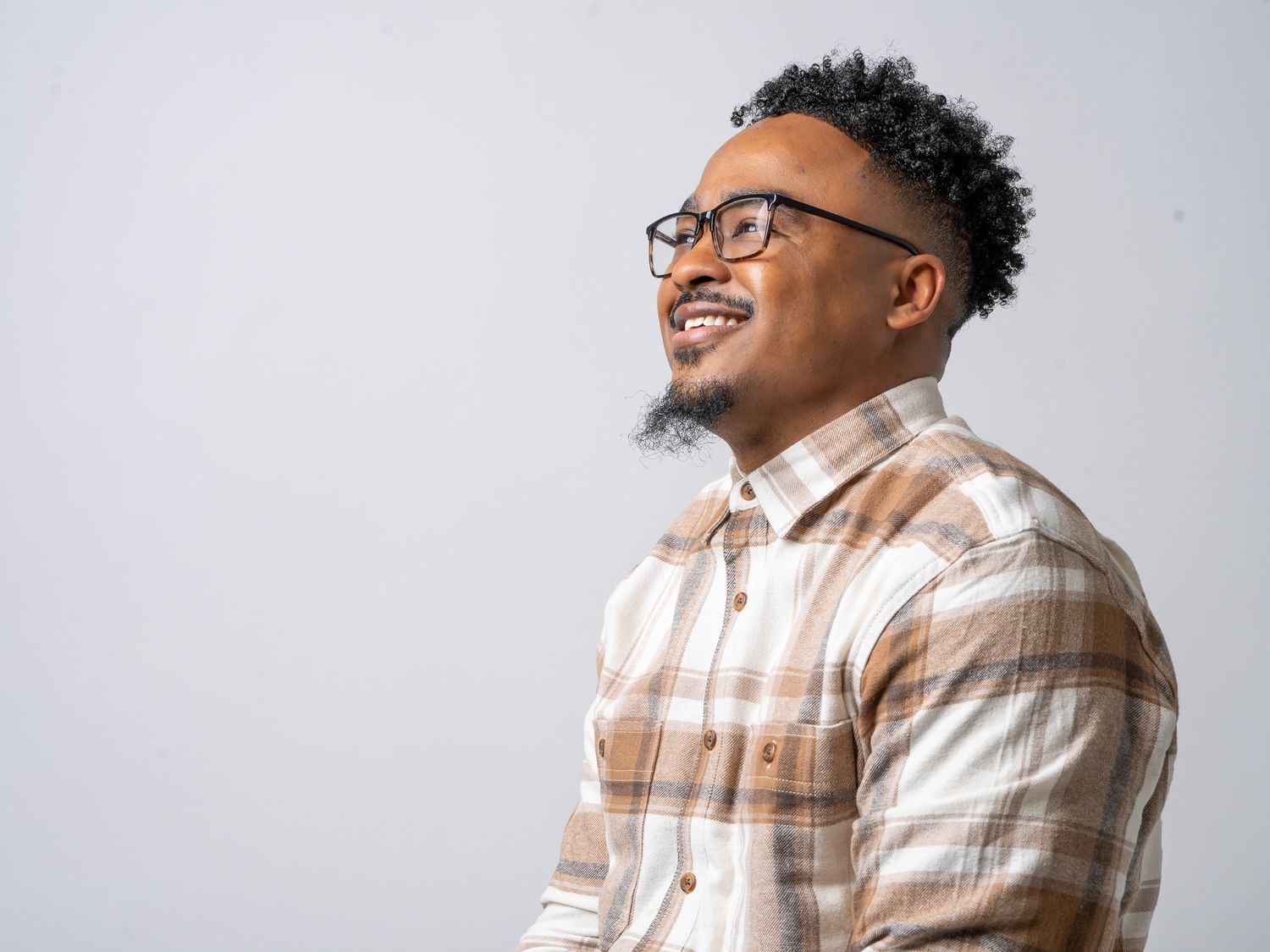 Studio portrait of person in plaid shirt smiling against light background.