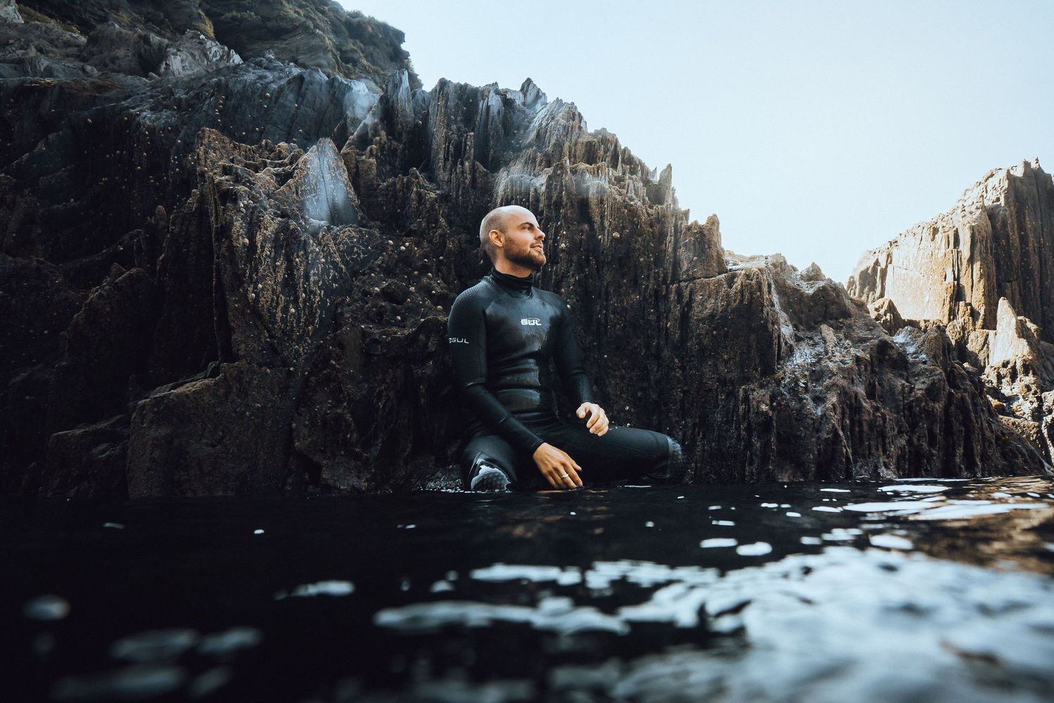Adventure seeker explores dramatic rocky coastline with dark waters and jagged cliffs.