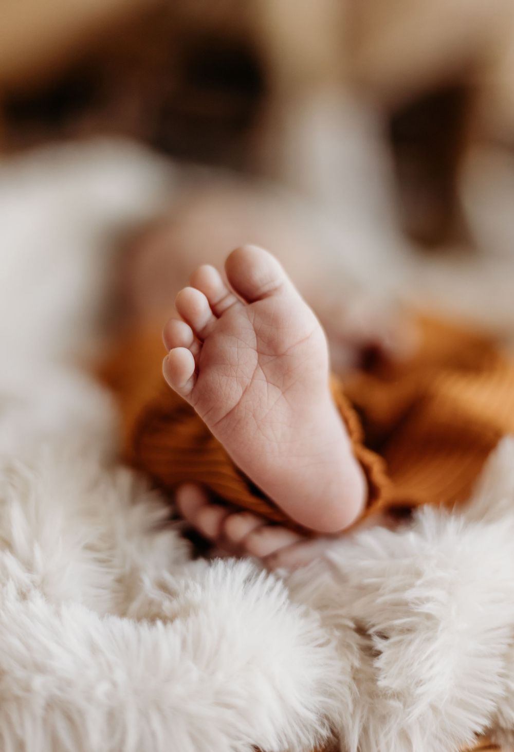 Close-up of tiny baby feet resting on soft white fur blanket.