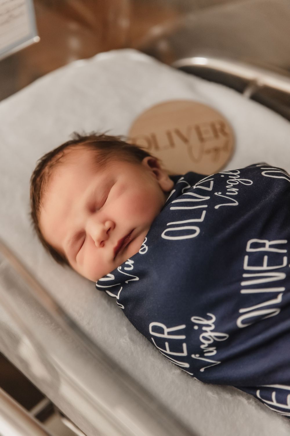 A sleeping newborn wrapped in a navy blue personalized swaddle blanket.