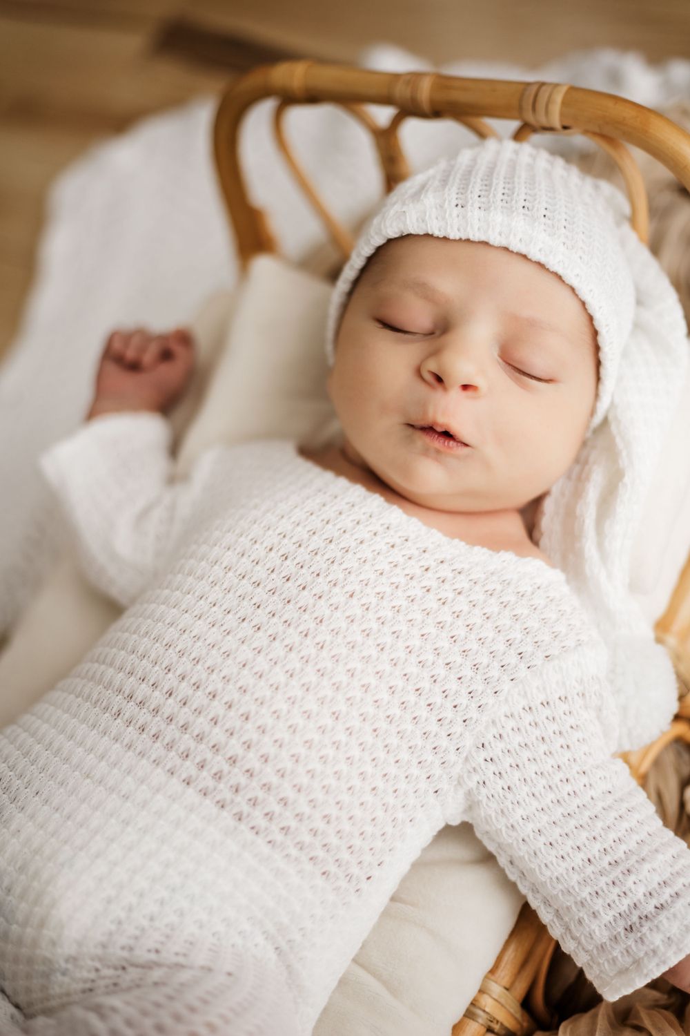 Peaceful sleeping newborn in white knit outfit on wicker bassinet.