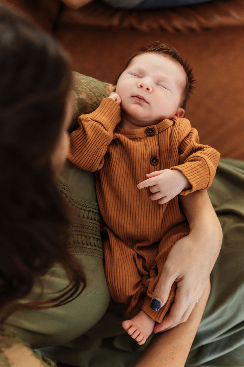 Sleeping newborn wearing ribbed rust-colored outfit on olive green fabric.