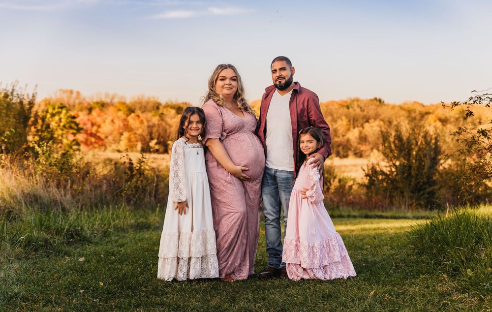 Family maternity photo session in a golden field at sunset with warm autumn colors.