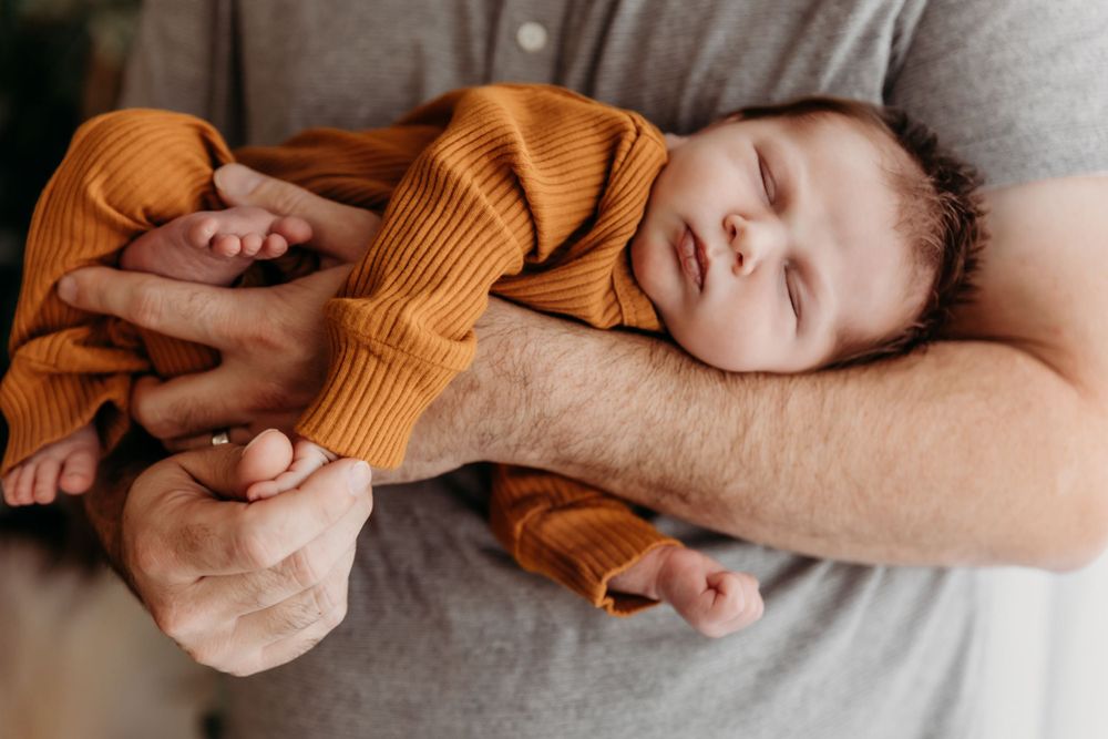 Intimate moment of baby sleeping on parent in soft indoor lighting.