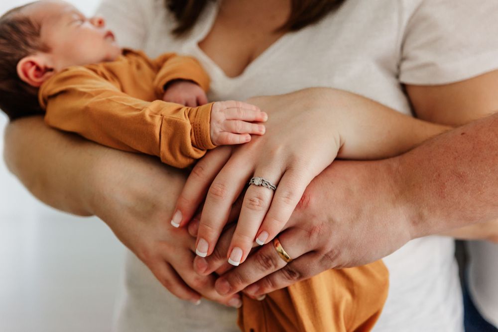 Close-up of hands holding a sleeping baby wearing an orange outfit.