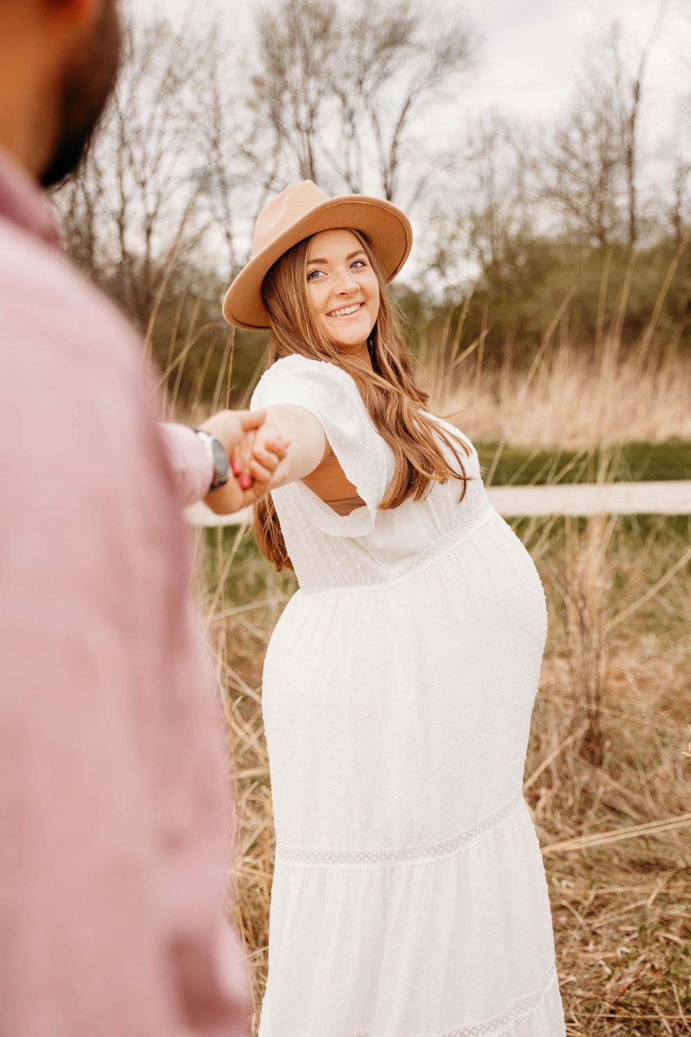 Dreamy outdoor maternity photos in a field with woman wearing white dress and brown hat.