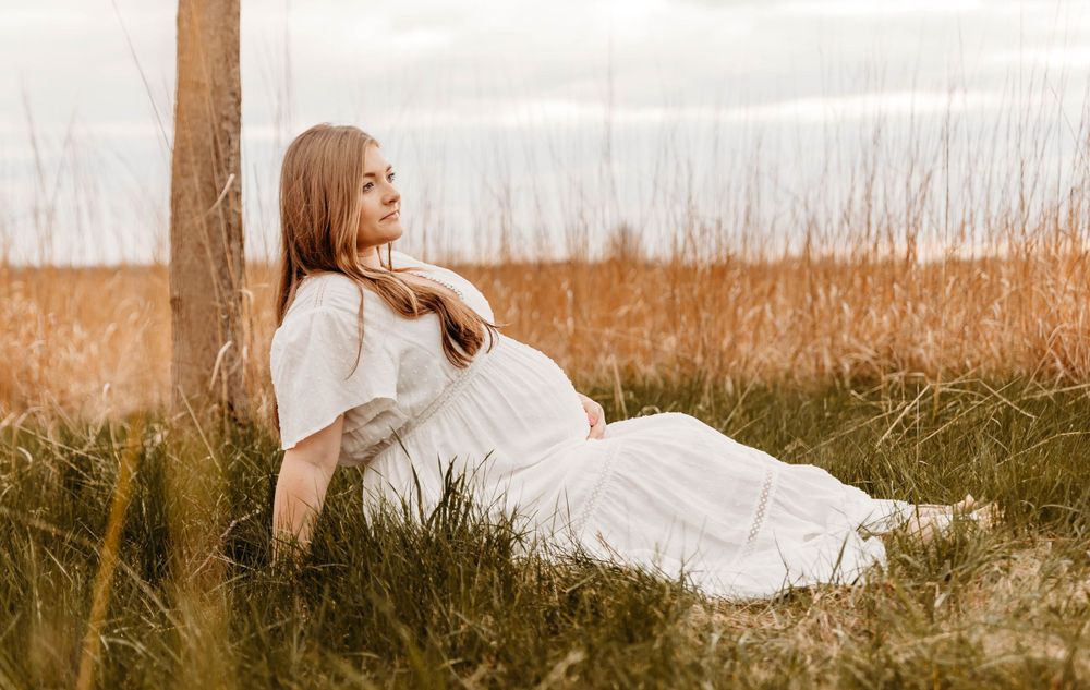 Serene maternity photography session in natural setting with tall grass and overcast sky.