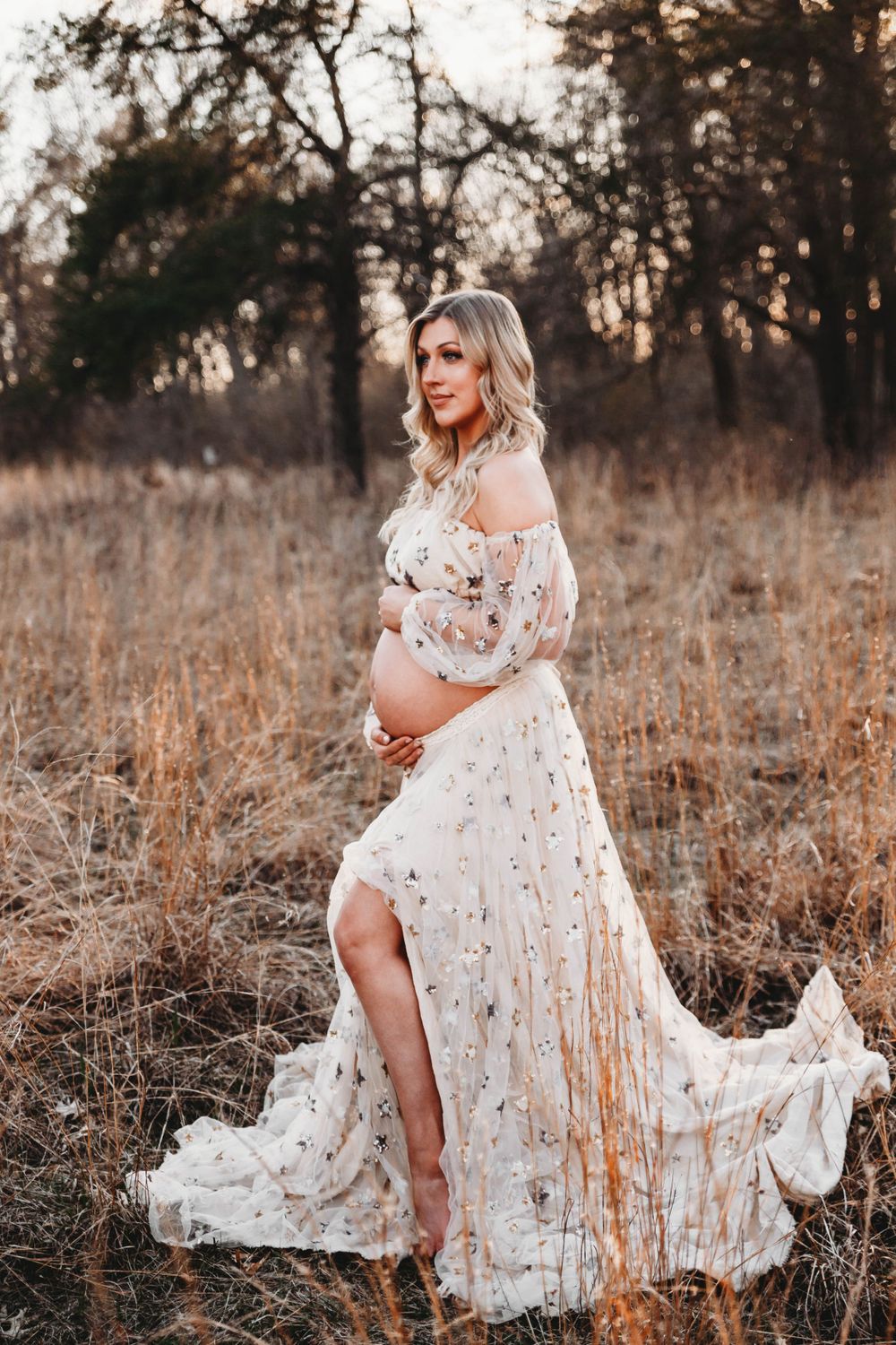 Elegant maternity photos featuring a white embroidered dress against dried grass and trees at dusk.