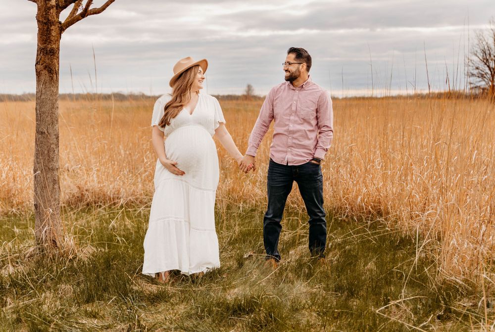 Romantic maternity photoshoot in golden field with couple in white dress and pink shirt.