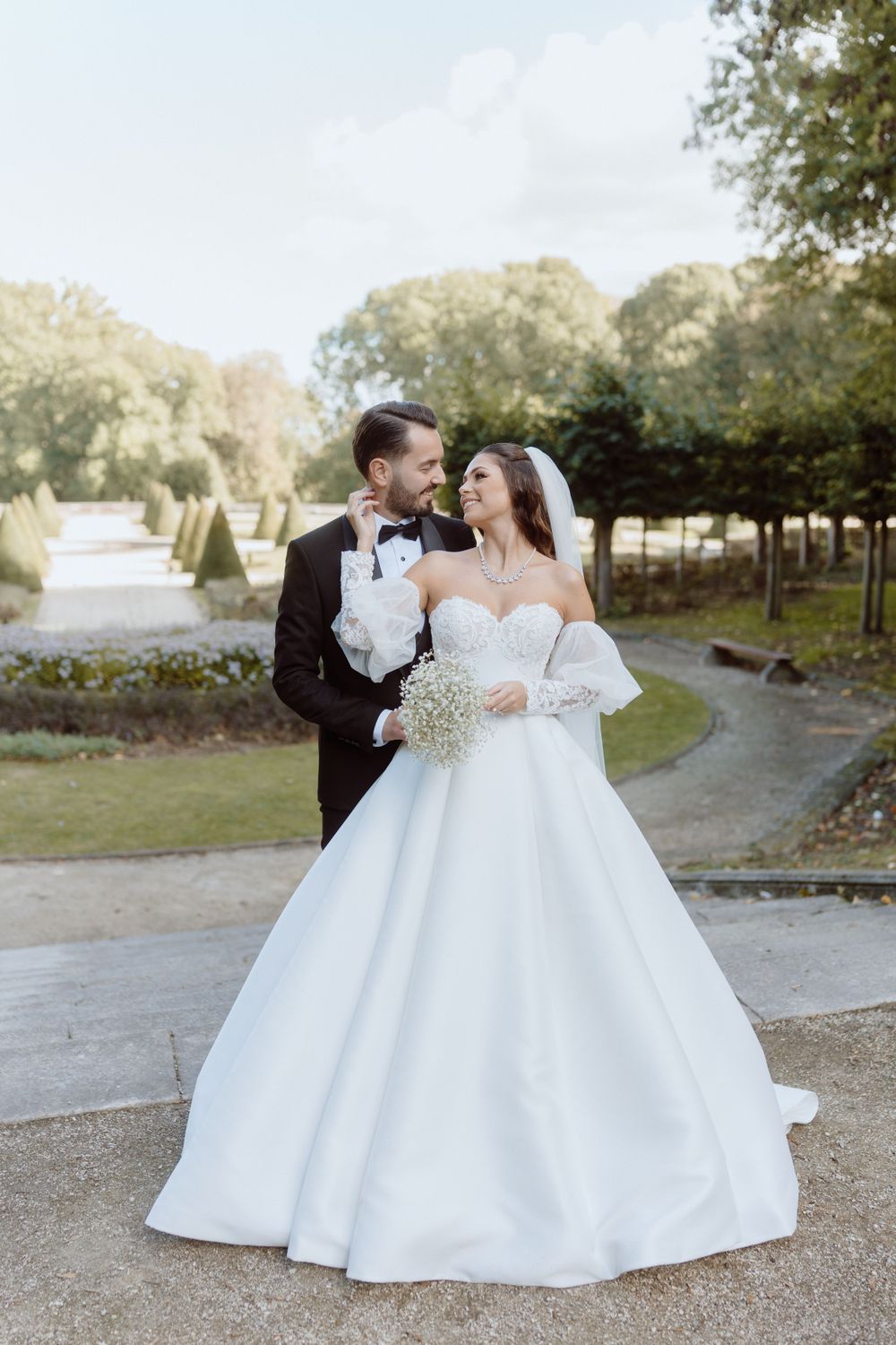 Elegant wedding couple on garden path with bride in princess ballgown and groom in classic tuxedo.