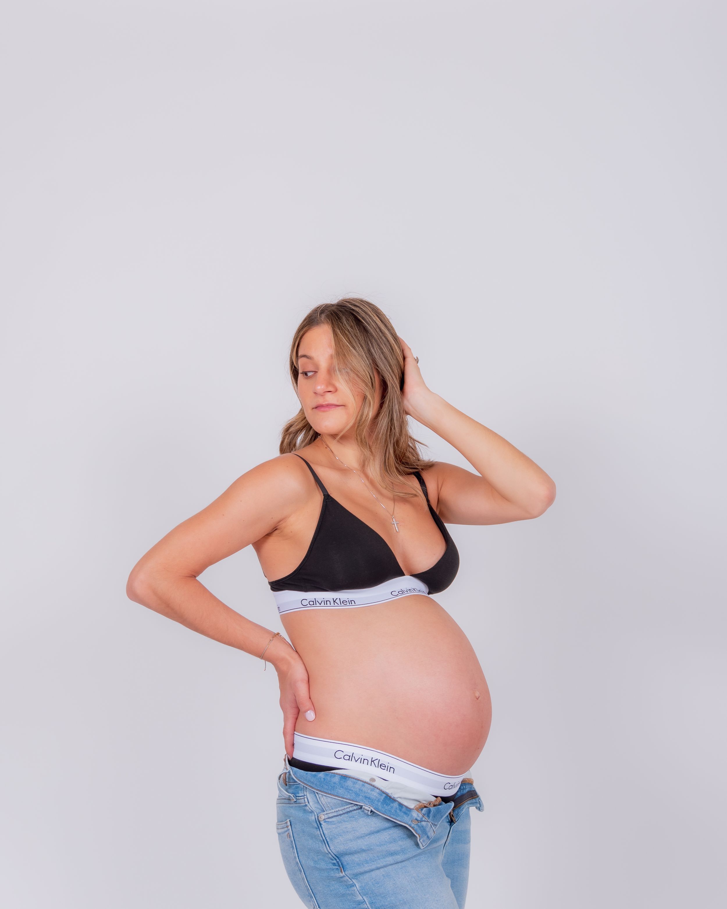 Side view of an expectant mother in black bra and jeans showing her pregnant belly.